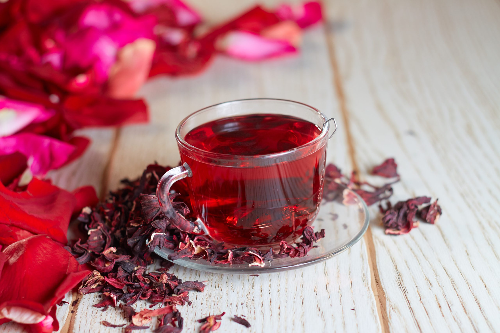 A glass cup of hibiscus tea surrounded by dried petals